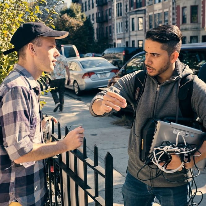 Two men standing side by side on a sidewalk talking